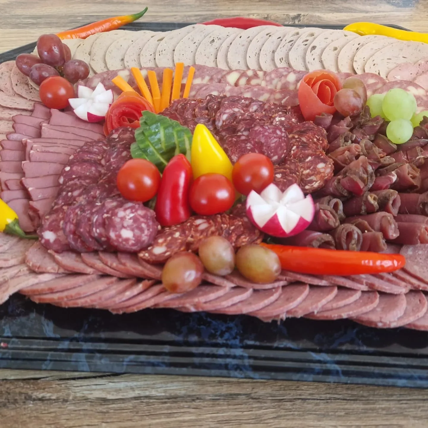 Liebevoll angerichtete Fleisch- und Wurstplatte mit Gemüse und Trauben